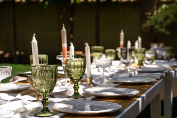 The table is set for a good party. The table is set. Empty plates and unusual glasses. Vintage tray and candleholder and vases with beautiful flowers. Everything for a celebration