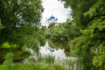 Domes and towers of holy bogolyubovsky monastery  among green trees foliage reflects in lake waters summer landscape