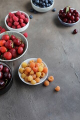 Many different ripe juicy berries in plates on the table. Summer flat lay. Raspberries, strawberries, cherries, cherries, blueberries.