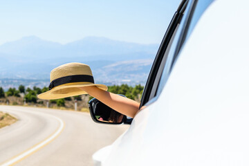 Woman driving a car holding straw hat from the open window. Trip on the serpentine road in the mountains. Summer vacation