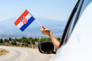 Woman holding Croatia flag from the open car window driving along the serpentine road in the mountains. Concept - 517346744