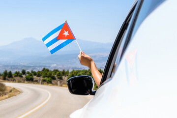 Woman holding Cuba flag from the open car window driving along the serpentine road in the mountains. Concept