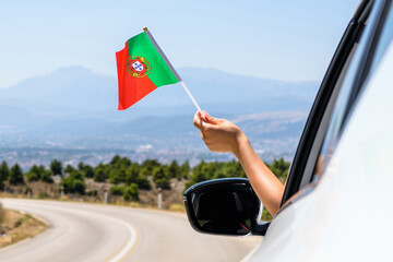 Woman holding Portugal flag from the open car window driving along the serpentine road in the mountains. Concept