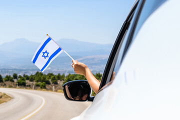 Woman holding  Israel flag from the open car window driving along the serpentine road in the mountains. Concept