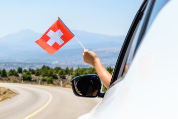 Woman holding Switzerland flag from the open car window driving along the serpentine road in the...