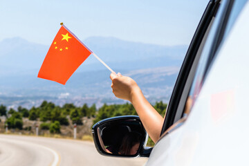 Woman holding China flag from the open car window driving along the serpentine road in the mountains. Concept