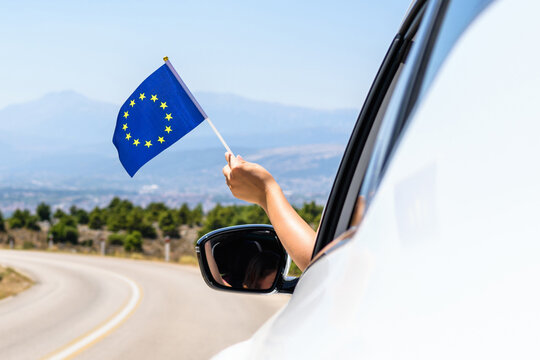 Woman holding European Union flag from the open car window driving along the serpentine road in the mountains. Concept
