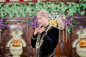 The groom wears Javanese traditional clothes, black and blangkon clothes and a jasmine necklace at the wedding. Beskap is traditional heritage clothing from Java, Indonesia