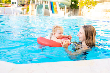 mom and baby in an inflatable circle in the pool with water slides in the summer have fun swimming, relaxing and spending time, mom teaches the child to swim