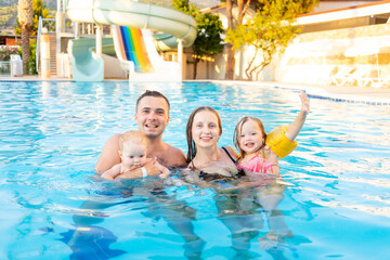 Obraz na płótnie Canvas happy family mom, dad and two children are swimming in the pool with water slides and having fun on vacation, smiling and laughing
