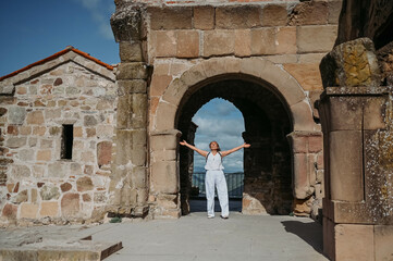 Happy senior traveler woman tourist posing outdoors in ancient Europe fortress ruins. Mature female arms outstretched. Retired old people summer holiday vacation, active lifestyle freedom concept