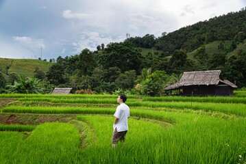 Man stand alone to relax and sightseeing view of paddy filed and wooden hut at Thailand