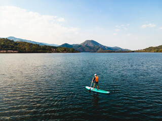 Young man stand the paddle board in the lake among mountain view