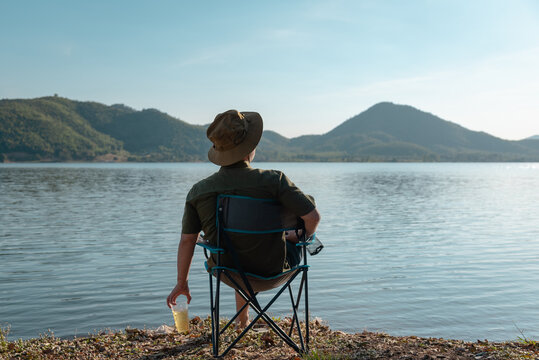 The man relax on vacation with beer and sit at champing chair among lake and mountain view, Thailand