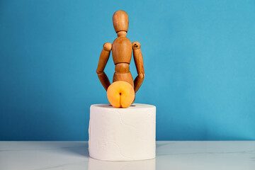 Digestion aid concept. Apricot in the form of buttocks. The wooden man sits on a roll of toilet...