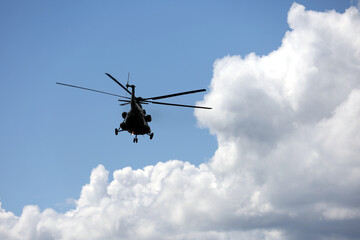 Fototapeta na wymiar Silhouette of military helicopter Mi-8 (NATO codification: Hip) in flight on background of blue sky and white clouds