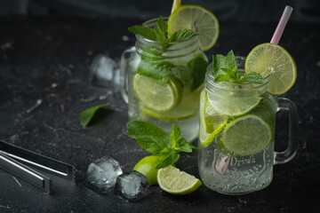 Refreshment mojito cocktail with mint and lime in a glass mug on a black background. Cold summer drink with ice