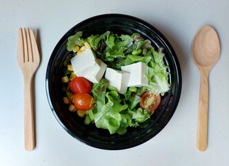 Japanese tofu salad in black plastic bowl.
