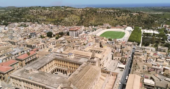 Zoom in aerial view of Noto, the ancient historical baroque Sicilian city in Italy, crossing a soccer field stadium.