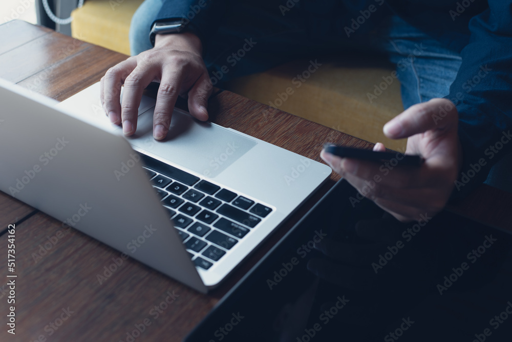 Wall mural man working on laptop and using mobile phone with digital tablet on wooden table at coffee shop, tel