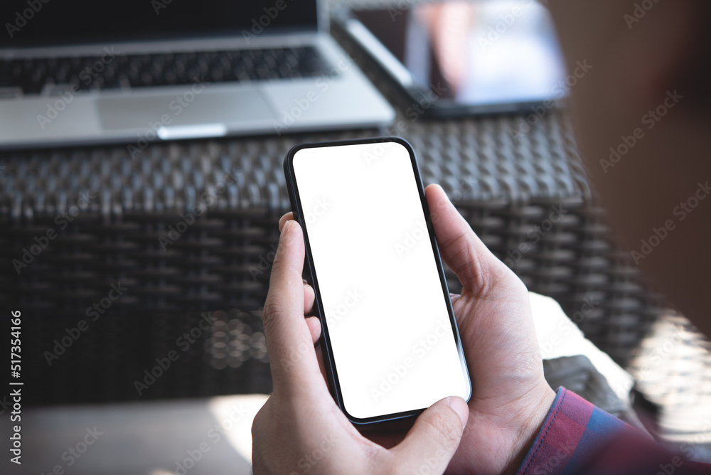 Wall mural Cell phone blank white screen mockup. Man hands holding, using mobile phone at office background, template for advertisement