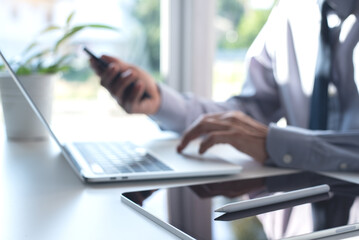 Businessman working on laptop computer and using mobile smart phone with digital tablet on white office table, blurred background