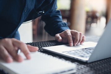 Business man hand writing on notepad, working on laptop computer on table at coffee shop. Student...