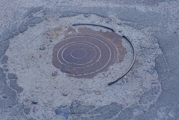 Fototapeta na wymiar one brown rusty iron sewer manhole lies in gray and sand and asphalt on the road in the street