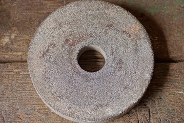 one old stone gray grinding wheel lies on a brown wooden table in a workshop