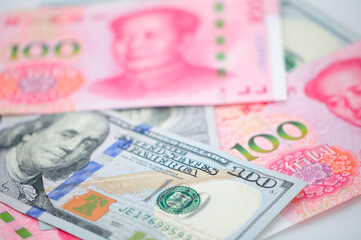 Chinese 100 Renminbi and 100 U.S. dollar bills piled on a white background.