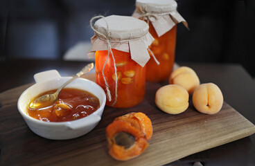 Apricot jam in glass jars on a wooden surface, a small white plate with jam and a miniature spoon....
