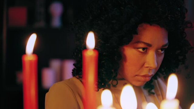 Frightful African American witch gazing through burning candles, psychic power