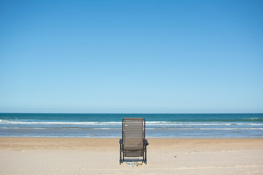 empty sun lounger seen from behind on the sand with the sea in front of it. Buzios Brazil Horizontal