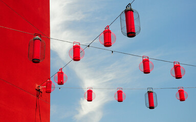 A red building exterior and red lanterns hanging from wires near the chinatown metro station in Los Angeles California on a sunny blue sky day.
