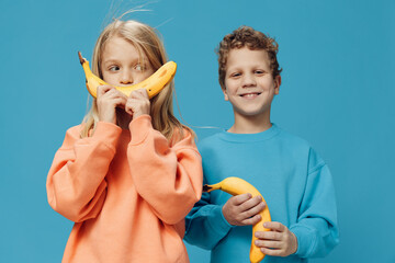 happy joyful children boy m girl of school age stand on a blue background and joyfully hold bananas...