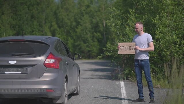 a man catches a passing car, the sign says America