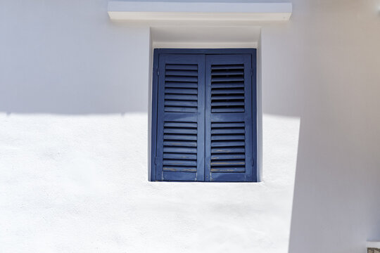 white painted greek house wall with blue wooden window shutters closed, minimalism concept, light and shadow