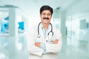 Portrait happy indian male doctor with stethoscope standing cross arms looking at camera,...