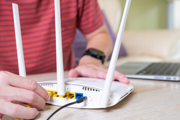 Selective focus at router. Internet router on working table with blurred man connect the cable at...
