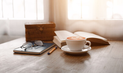 Close up view, white coffee cup with smartphone, notebook and pen on table, after get up in the morning on holiday with breakfast, vintage color tone and soft light from window on background