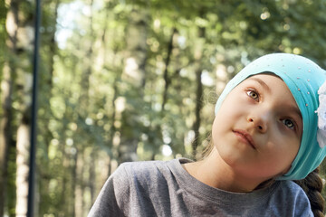 The girl child looks in the direction close-up, the rays of the sun shine through the trees and leaves. Nature walk