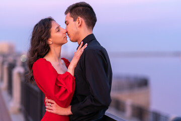 a guy and a girl kiss at sunset on the embankment near the river