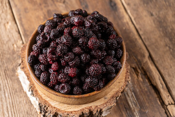 The black berry is a hybrid of raspberries and blackberries. Berries in a wooden bowl on the table....