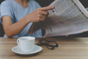 Fototapeta na wymiar A cup of coffee,glasses on the wood table and woman read a newspaper.