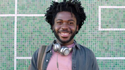 Portrait of a young smiling student with headphones outside. Face of a trendy african man with afro and dreadlocks relaxing and looking happy. Face of casual male enjoying a break from work or class