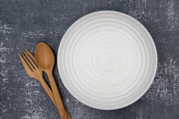 A white round empty plate with fork and spoon on dark background for food and ingredient concept set up