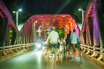 group of men riding the pedicab (Cycle rickshaw) on the Truong Tien bridge at night. Hue . Vietnam