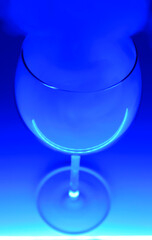 A glass with an alcohol vapors of vodka in a neon blue light on a blue background. Alcohol cocktail. Selective focus.