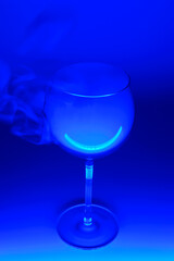 A glass with an alcohol vapors of vodka in a neon blue light on a blue background. Alcohol cocktail. Selective focus.
