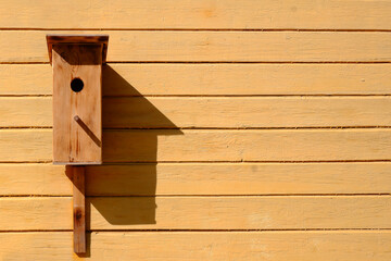 A small wooden birdhouse on a pole on a yellow background of wooden boards.Care and care of birds.Copyspace